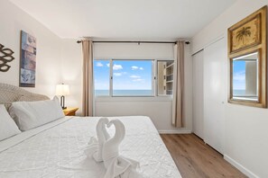 A hotel room with a bed, a nightstand, a lamp, a window with curtains, and a view of the sea. - Pinnacle Port, C2-301 (Panama City Beach)