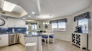 A modern kitchen with white cabinetry, a marble countertop, and a dining area with white chairs and blue cushions. - ALL NEW Family Jewel Myrtle Beach (MYRTLE BEACH)