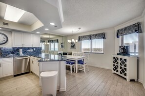 A modern kitchen with white cabinetry, a marble countertop, and a dining area with white chairs and blue cushions. - ALL NEW Family Jewel Myrtle Beach (MYRTLE BEACH)