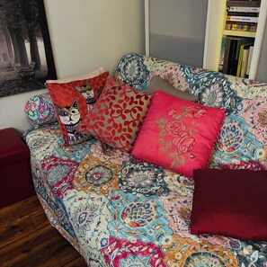 Ein Sofa mit gemusterten Bezügen, ein rotes Kissen mit Katzenmotiv und ein rotes Kissen mit Blumenmuster.