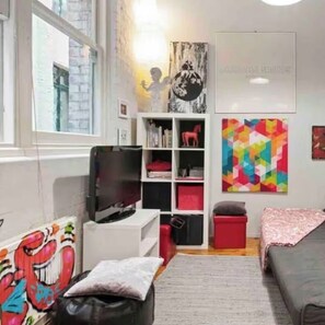 Ein modernes Wohnzimmer mit Fernseher, Bücherregalen, einem farbenfrohen abstrakten Gemälde und einem Sofa.