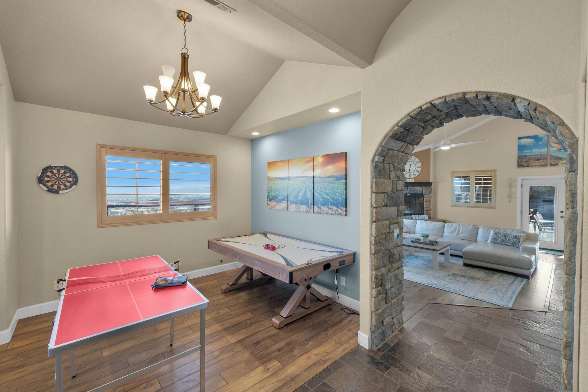 A room with a ping pong table, foosball table, and a stone archway leading to a living area with a sofa and coffee table.