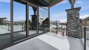 A modern building with large glass windows, stone pillars, and metal chairs on a snowy deck. - Luxury 4 bedroom chalet ski in/out (Beaverdell)