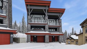 A multi-story building with a stone facade, large windows, and red garage doors. - Luxury 4 bedroom chalet ski in/out (Beaverdell)