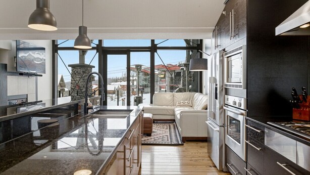 A modern kitchen with a central island, stainless steel appliances, and a large window offering a view of the outdoors. - Luxury 4 bedroom chalet ski in/out (Beaverdell)