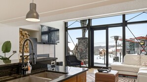 A modern kitchen with a large island, a stone wall, and a TV mounted above the counter. - Luxury 4 bedroom chalet ski in/out (Beaverdell)