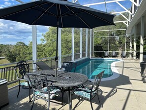Un espace extérieur abrité avec une piscine, une table et des chaises, et une vue sur les arbres.