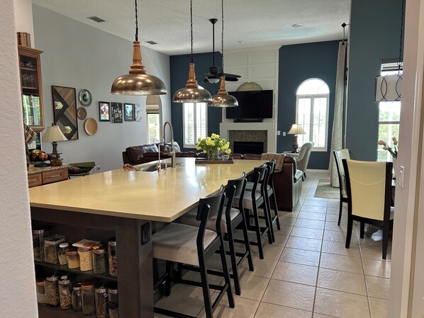A spacious kitchen with a large island, pendant lighting, and a fireplace.