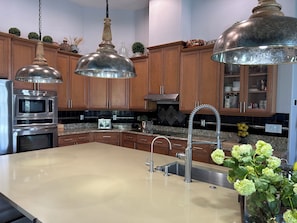 A modern kitchen with stainless steel appliances, wooden cabinets, and pendant lighting.