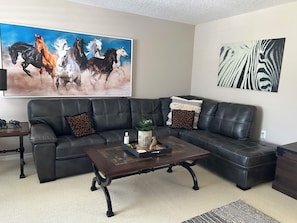 Un salon avec un canapé en cuir noir, une table basse et un grand tableau représentant des chevaux.