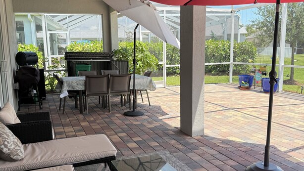 A covered patio area with outdoor furniture, a grill, and a ceiling fan.