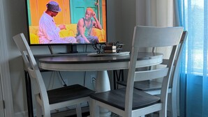 A dining area with a television, white chairs, a round table, and a patterned rug.