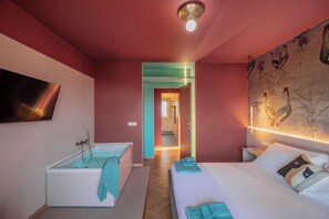 Ein modernes Hotelzimmer mit Badewanne, einem Bett mit Handtüchern, einem Flachbildfernseher und einem Wandgemälde.