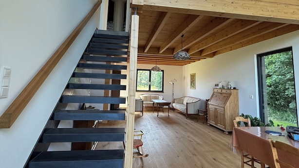 Ein modernes Interieur mit einer Holztreppe, einem Essbereich und großen Fenstern.