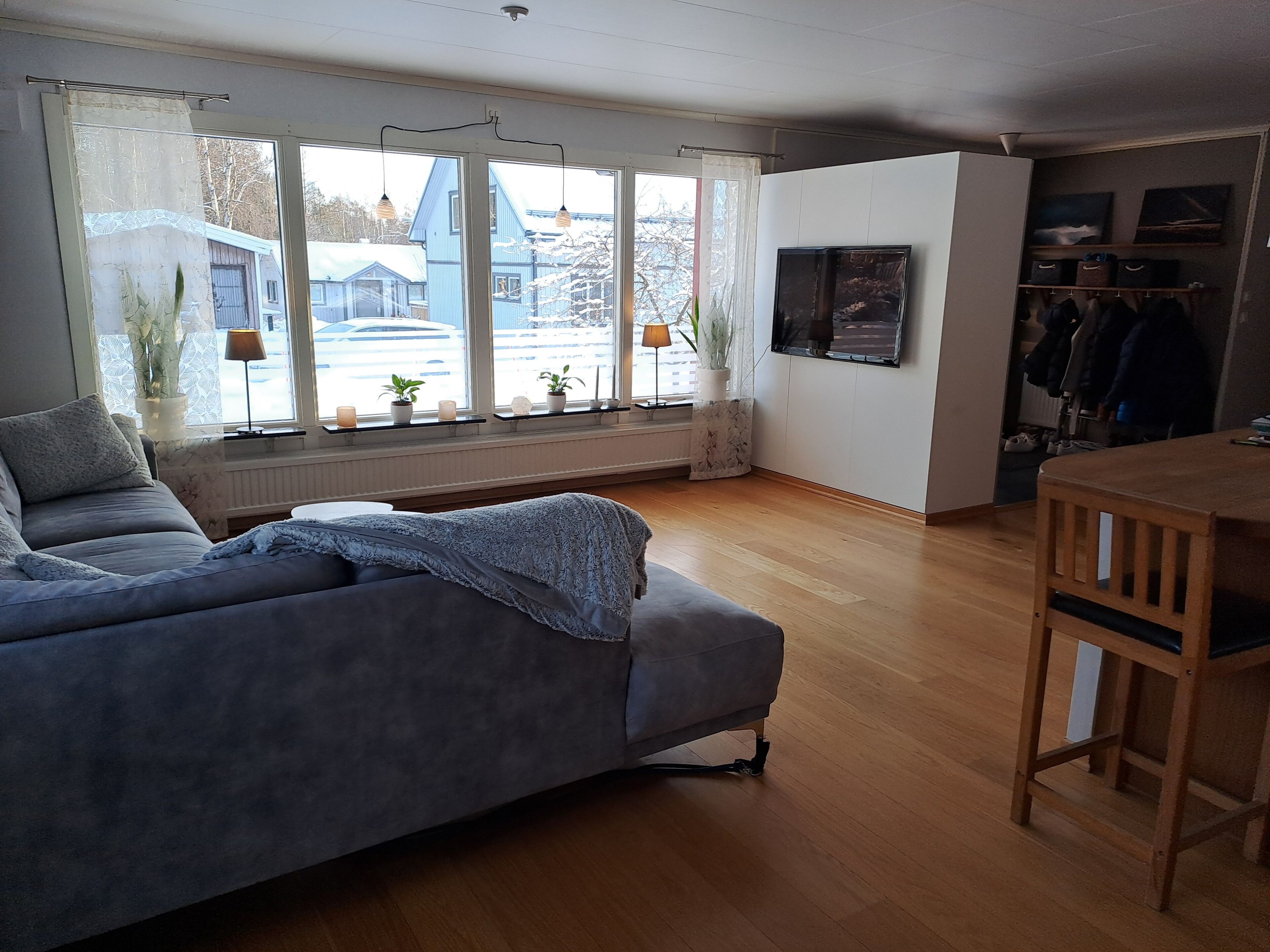 A living room with a sofa, a dining table, and a TV mounted on the wall.