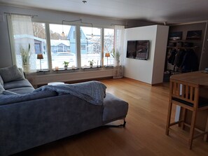 A living room with a sofa, a dining table, and a TV mounted on the wall.