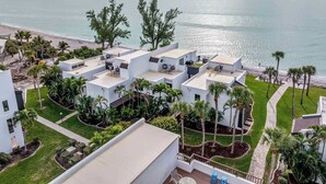 A coastal hotel with multiple white buildings, rooftop terraces with outdoor furniture, and palm trees. - Gulf View Condo - Beach Access - Rooftop Deck (Englewood)