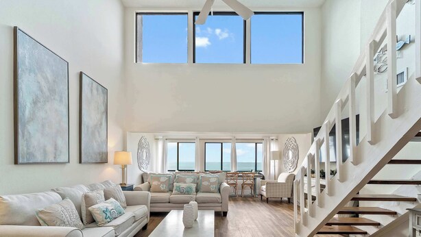 A spacious living area with a high ceiling, large windows, a staircase, and a view of the ocean. - Gulf View Condo - Beach Access - Rooftop Deck (Englewood)