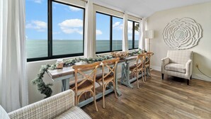 A dining area with a view of the ocean, a round wall decoration, and a plaid armchair. - Gulf View Condo - Beach Access - Rooftop Deck (Englewood)