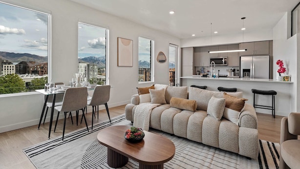 Ein modernes Wohnzimmer mit Sofa, Esstisch und Stühlen, einer Küchenzeile und großen Fenstern mit Blick auf die Stadt.
