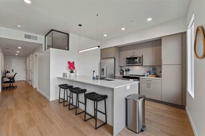 A modern kitchen with a central island, bar stools, stainless steel appliances, and a trash can. - Stylish 2-Bedroom, 2-Bath Salt Lake City Apartment with Balcony (Salt Lake City)