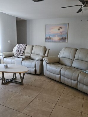 A living room with two leather sofas, a round coffee table, and a ceiling fan. - Serene 2-bedroom house with AC in charming North Port (North Port)