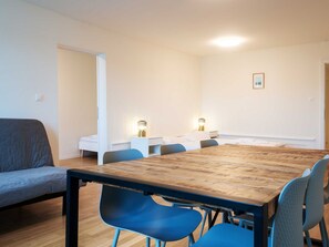 Een moderne kamer met een houten eettafel, blauwe stoelen, een grijze bank en een wit bed.