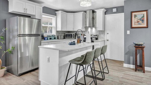 A modern kitchen with white cabinets, stainless steel appliances, a central island with bar stools, and a chandelier. - Pet-Friendly Home - Sleeps 6 - Walkable Lakewood (Lakewood)