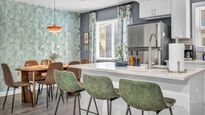 A modern kitchen with white cabinets, a stainless steel refrigerator, and a dining area with a round table and chairs. - Pet-Friendly Home - Sleeps 6 - Walkable Lakewood (Lakewood)