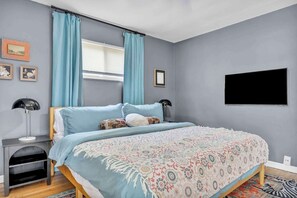 A bedroom with a bed, curtains, a TV, and a nightstand. - Pet-Friendly Home - Sleeps 6 - Walkable Lakewood (Lakewood)