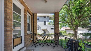 A covered porch with a table and chairs, a brick wall, a window, and a tree. - Pet-Friendly Home - Sleeps 6 - Walkable Lakewood (Lakewood)