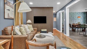 A modern living room with a sofa, armchair, TV, and dining area with chairs and a table. - Pet-Friendly Home - Sleeps 6 - Walkable Lakewood (Lakewood)