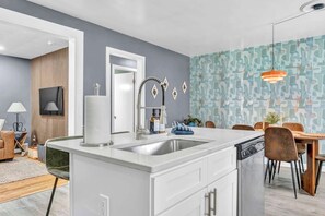 A modern kitchen with a central island, a dining area with wooden chairs, and a patterned wall.