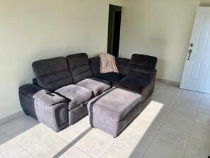 A grey sectional sofa with a blanket, a white door, and tiled flooring. - Beach House in Playa Dorada with Bay Club and Swimming Pools | WIFI | Pets (Vacamonte)