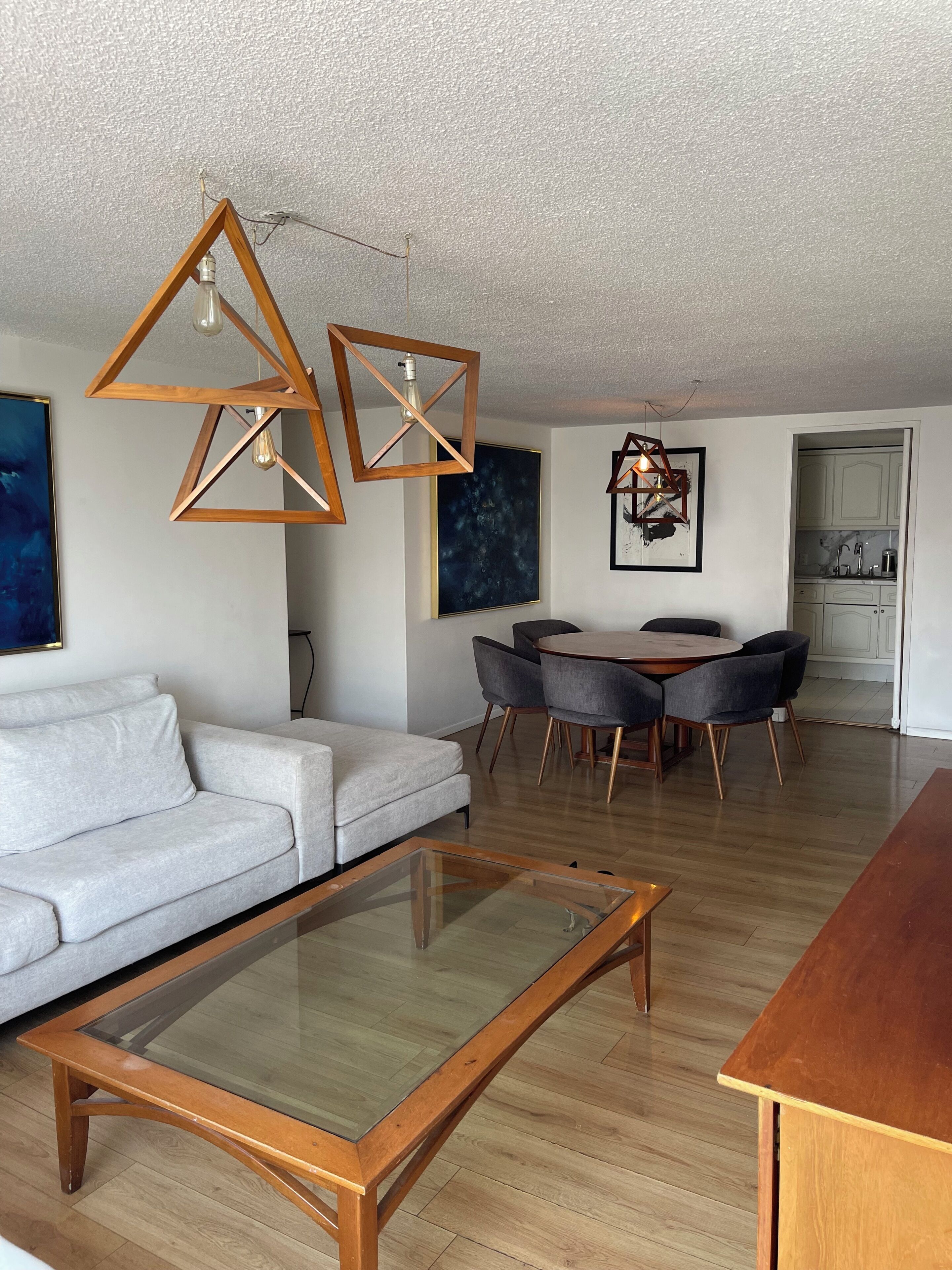 A modern living room with a sofa, a glass-top coffee table, a dining area with chairs, and a kitchen in the background.