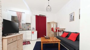 Een compacte leefruimte met een televisie, houten meubels, een rood gordijn en een kleine kitchenette.