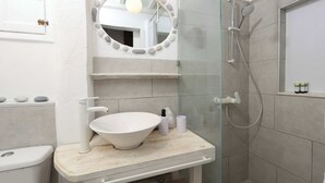 Een badkamer met een wit wastafel, een spiegel met een stenen omlijsting, een douche en een toilet.