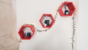 Drie rode, zeshoekige planken op een witte muur, elk met verschillende spullen.