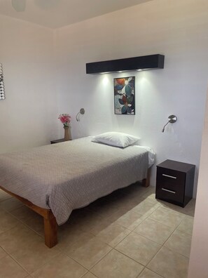 A bedroom with a bed, bedside tables, a wall-mounted artwork, and a small cabinet.