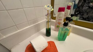 Ein Badezimmer mit einem weißen Waschbecken, einer Glasvase mit Blumen, einer Duschgel-Flasche und einer Shampoo-Flasche.