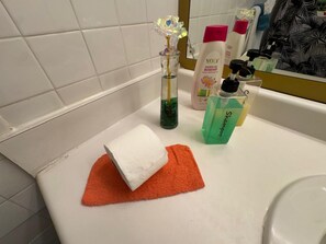 Ein Badezimmer mit einem weißen Waschbecken, einer Glasvase mit Blumen, einer Duschgel-Flasche und einer Shampoo-Flasche.