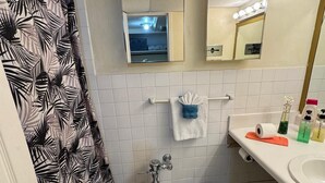 Ein Badezimmer mit Toilette, Waschbecken, Spiegel und einer Duschkabine mit Blätlemuster.