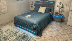 A neatly made bed with a blue bedspread, a bedside lamp, and a nightstand with a lamp. - Inlet Life -Private Dock/Pool- (Murrells Inlet)