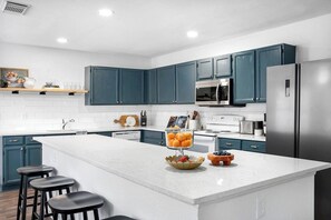 A modern kitchen with teal cabinets, a large island, stainless steel appliances, and bar stools. - Shady Oak: Pool, Hot Tub, Game Room | Sleeps 12 (Live Oak)