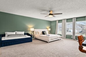 A bedroom with a bed, a chair, a ceiling fan, and a window with curtains. - Shady Oak: Pool, Hot Tub, Game Room | Sleeps 12 (Live Oak)