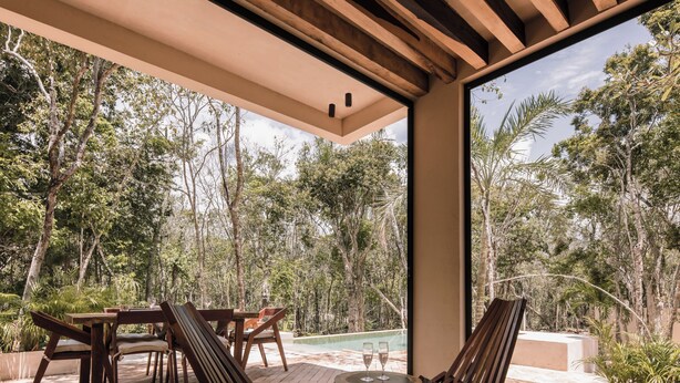 Eine Terrasse im Freien mit Holzmöbeln, einem Glastisch und Blick auf ein bewaldetes Gebiet.