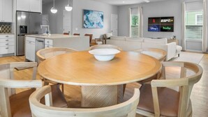 Una cucina moderna con mobili bianchi, un tavolo da pranzo con sedie, un lampadario a sospensione grande e una TV a schermo piatto che mostra servizi di streaming.