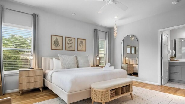 Una camera da letto con un letto, comodini, una panca, una ventola a soffitto e stampe botaniche incorniciate alle pareti.