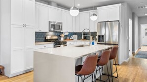 Una cucina moderna con mobili bianchi, elettrodomestici in acciaio inossidabile, un'isola centrale con sgabelli da bar e illuminazione a sospensione.