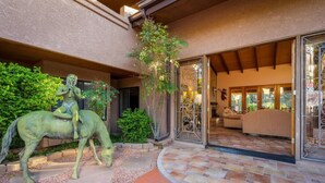 A building with a stone pathway leading to an open entrance, a statue of a person on a horse, and a well-lit interior with a sofa and a dining area. - Adobe Village Inn Painted Desert (Sedona)